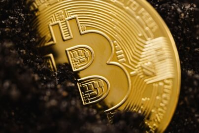 Close-up of a gold Bitcoin coin emerging from dark soil, representing digital currency growth.