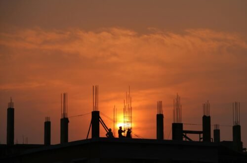 Silhouette of workers on a construction site against a vibrant sunset sky.